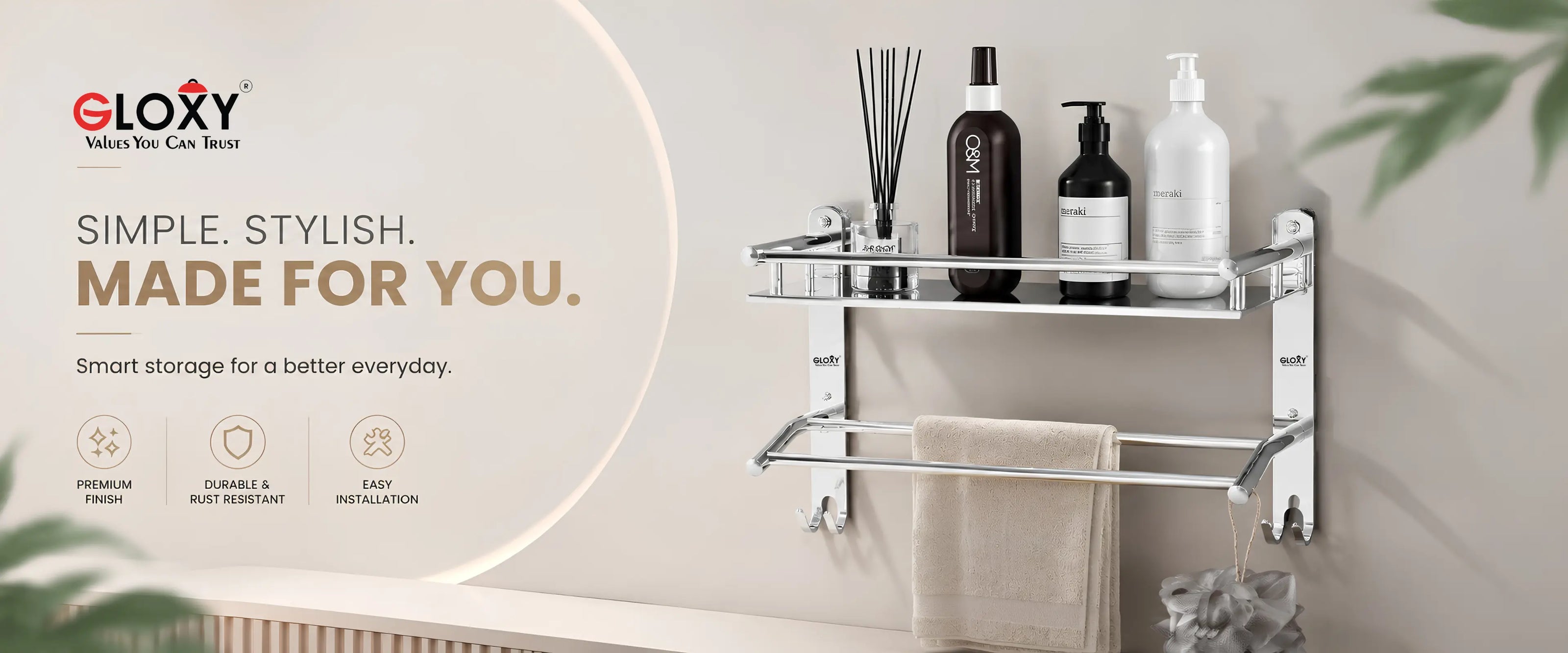 A wall-mounted double-tier bathroom shelf with a towel bar, shown installed on a beige wall in a bathroom setting. The shelf holds several toiletry bottles and a reed diffuser, with a beige towel hanging from the bar.
