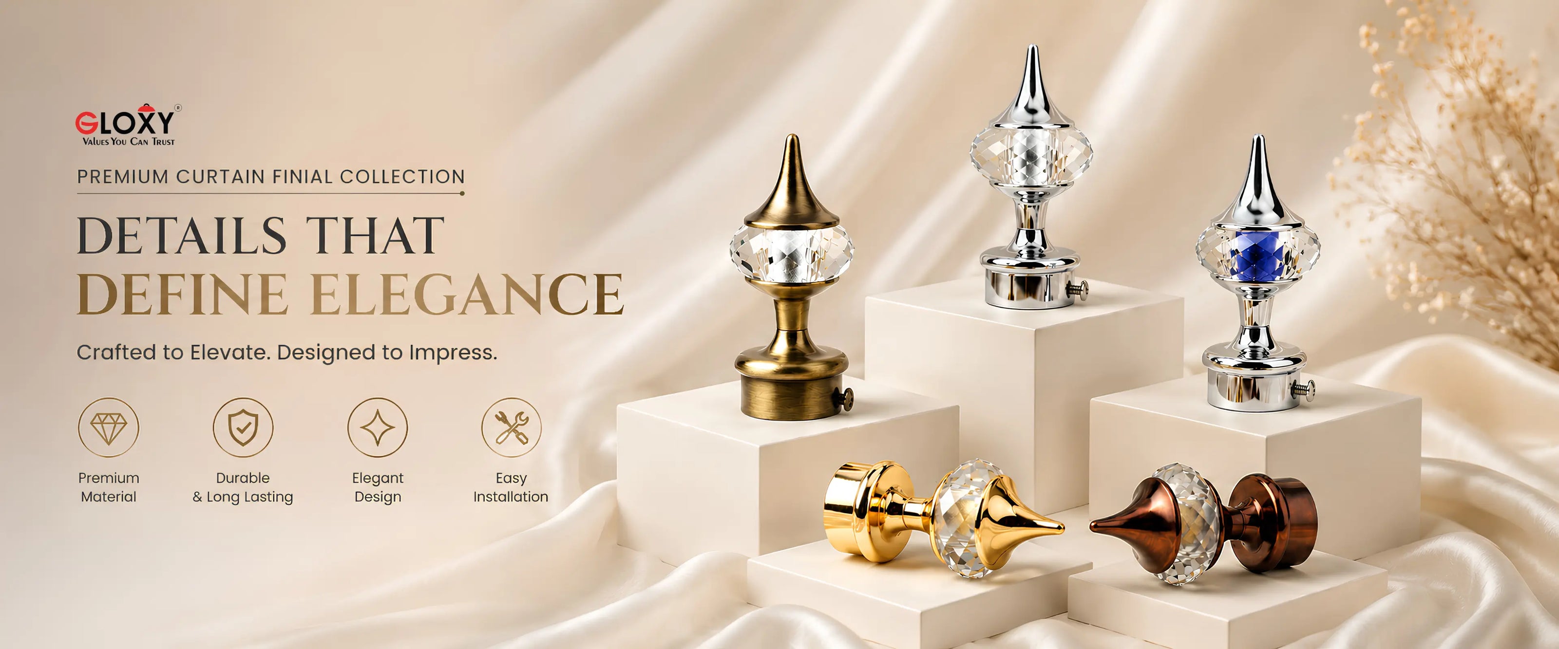 A promotional display of several curtain finials arranged on white pedestals against a draped beige fabric backdrop. The collection includes gold, silver, blue, and dark brown finials, with some featuring clear crystal-like spheres.