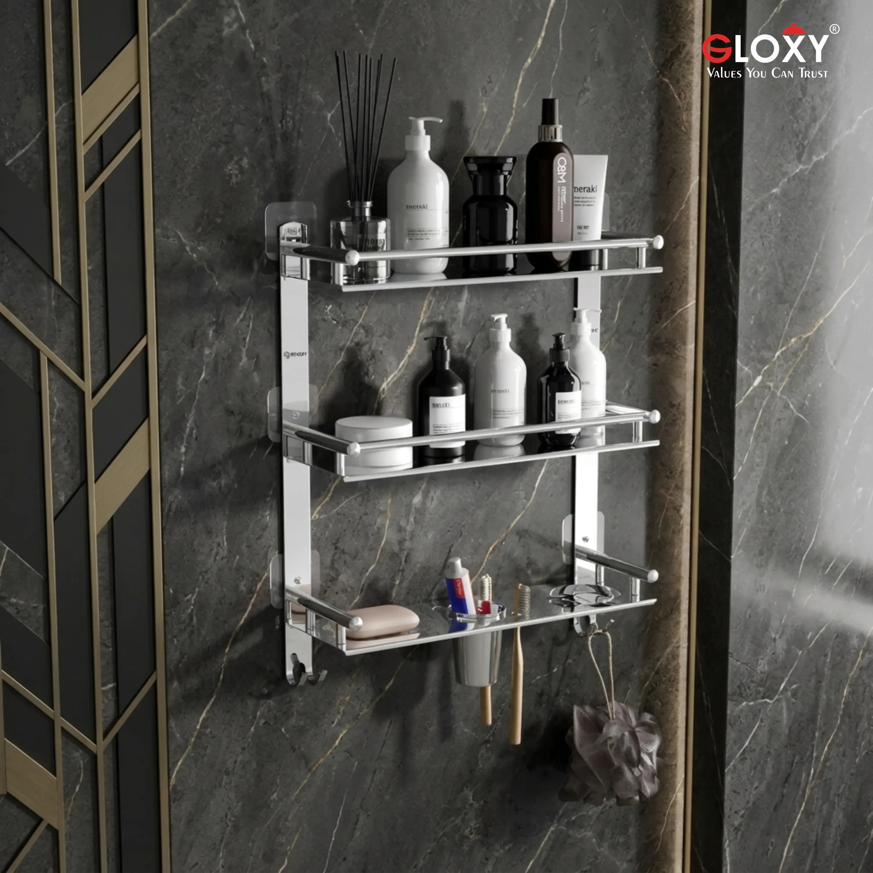A wall-mounted three-tier chrome bathroom shelf with bottles, jars, and toiletries displayed on a dark marble wall. The brand logo 'eLOXY' is visible in the top right corner.