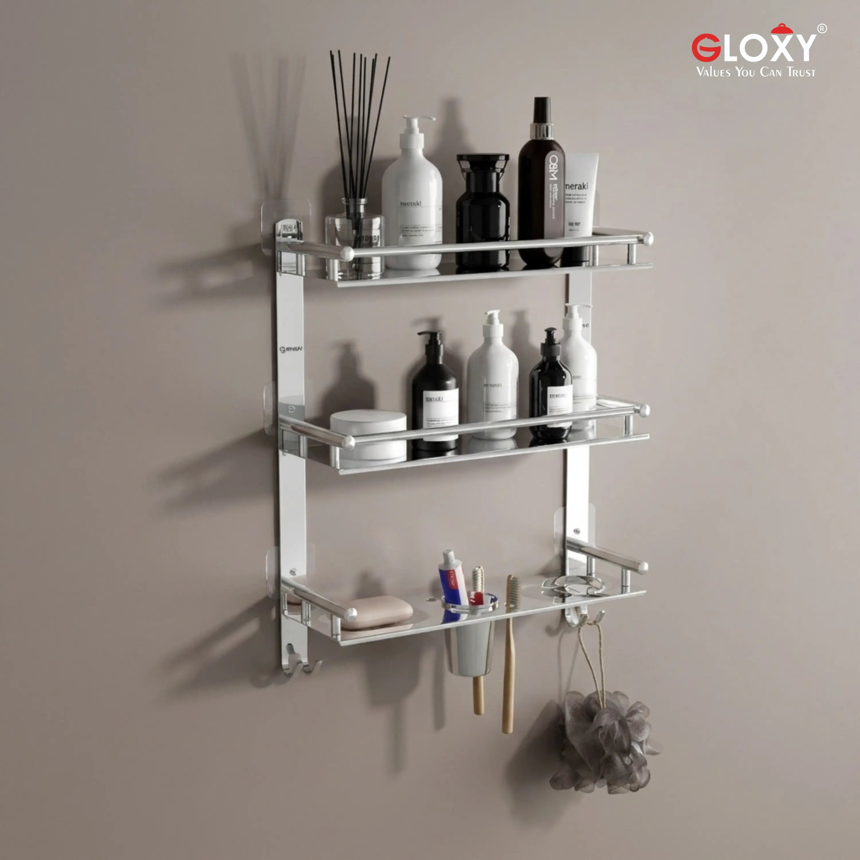 A three-tier wall-mounted glass shelf with chrome silver metal brackets, shown mounted on a beige wall and filled with bathroom toiletries. The brand logo 'ELOXY' is visible in the top right corner.